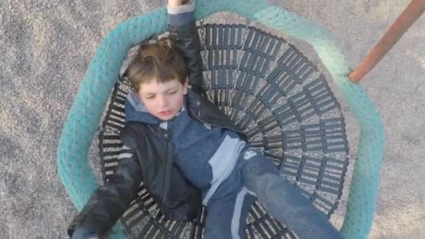 El niño yace en un columpio, levanta la pierna en la cámara — Vídeos de Stock