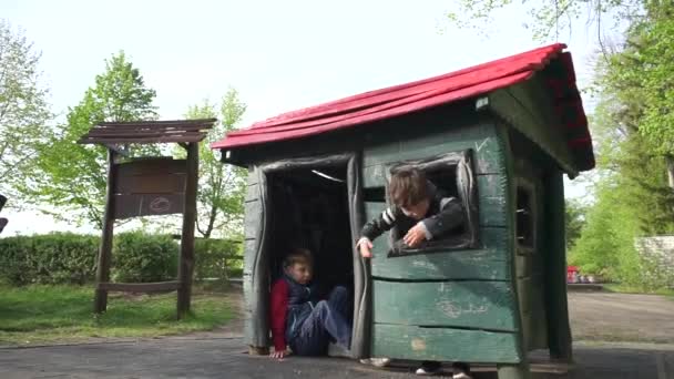 Zwei Kinder spielen in einem Spielzeughaus auf dem Spielplatz — Stockvideo