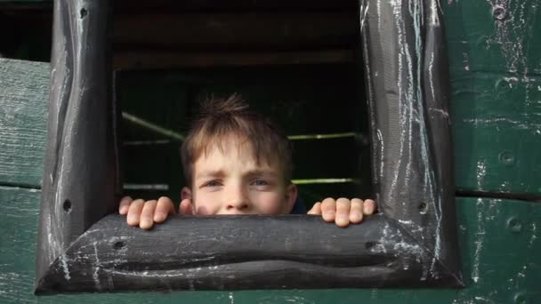 Мальчик вылезает из окна, машет пальцем, улыбается — стоковое видео