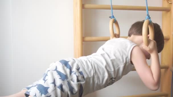 Хлопчик штовхає на гімнастичні кільця в тренажерному залі — стокове відео