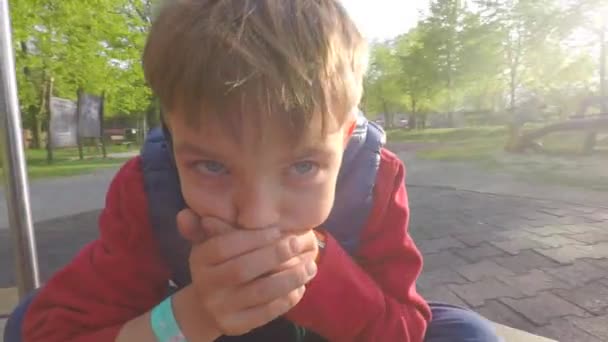 Мальчик едет на карусели, показывает, что он болен, закрывает рот руками — стоковое видео