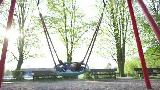 Kleiner Junge schläft in Schaukel auf Spielplatz — Stockvideo