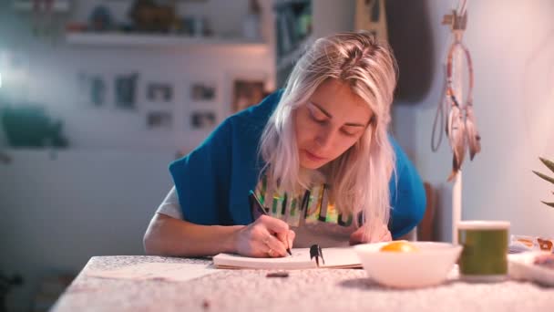 Блондинка малює за столом на кухні . — стокове відео