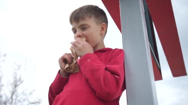 Jongen eet een broodje staand bij de pilaar — Stockvideo