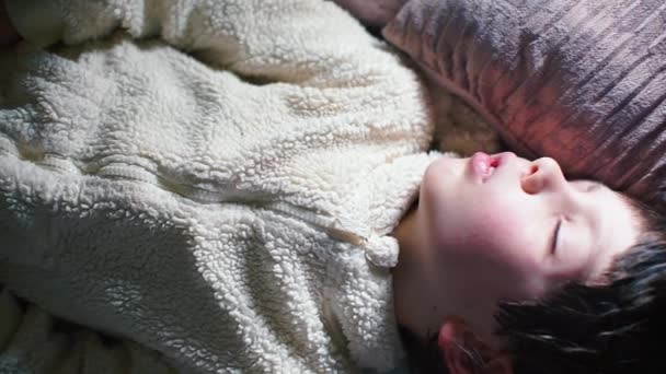 Bir okul çocuğu beyaz pijamalarıyla kanepede uyuyor.. — Stok video