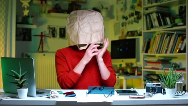 En galen sjuk man som sitter vid ett bord på kontoret. På hans huvud är en papperspåse. — Stockvideo