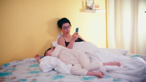 Eine junge Mutter liegt auf der Couch und benutzt ein Smartphone. — Stockvideo