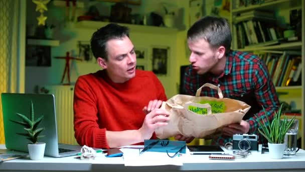 Δύο τύποι μιλούν για μια χάρτινη σακούλα σε ένα τραπέζι στο γραφείο.. — Αρχείο Βίντεο