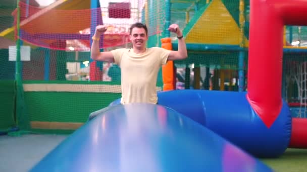 Un padre joven está sentado en un pueblo inflable en un parque infantil . — Vídeos de Stock