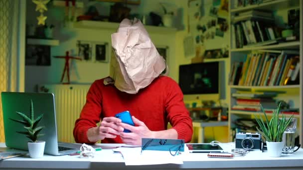 Ein Büroangestellter sitzt mit einer Papiertüte auf dem Kopf an einem Schreibtisch. — Stockvideo