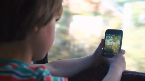 Un écolier monte dans un train près de la fenêtre. Dans les mains d'un smartphone . — Video