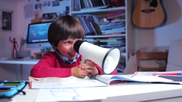 Boy sitting at the table smiles then shouts into a megaphone — Stock Video