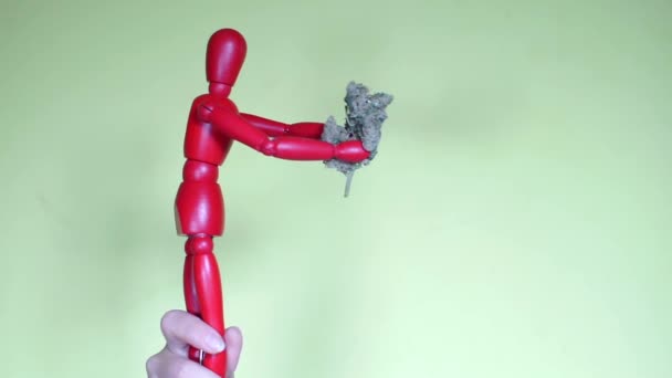Die Figur eines roten Mannes hält medizinische Marihuana-Knospen in seinen Händen — Stockvideo