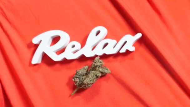 Bewegende witte belettering ontspannen en cannabis knop op rode stof in een coffeeshop — Stockvideo