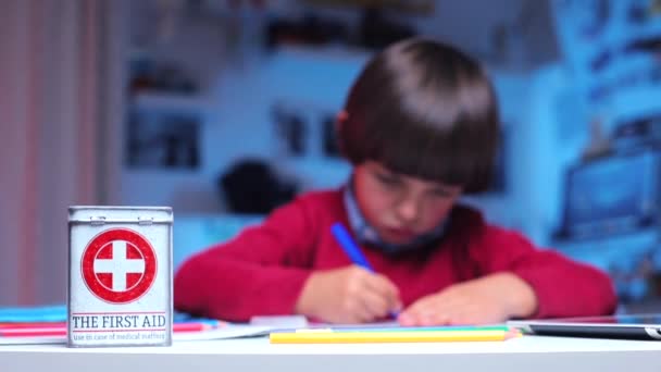 Auf dem Tisch liegt eine Schachtel mit der Aufschrift Erste Hilfe, auf dem Hintergrund ein Junge — Stockvideo