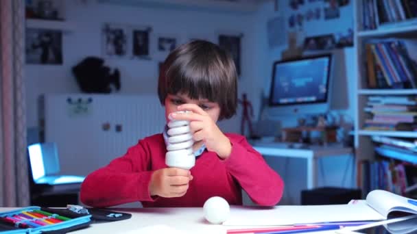 Portret kind onderzoeker onderzoekt een lamp in zijn handen — Stockvideo