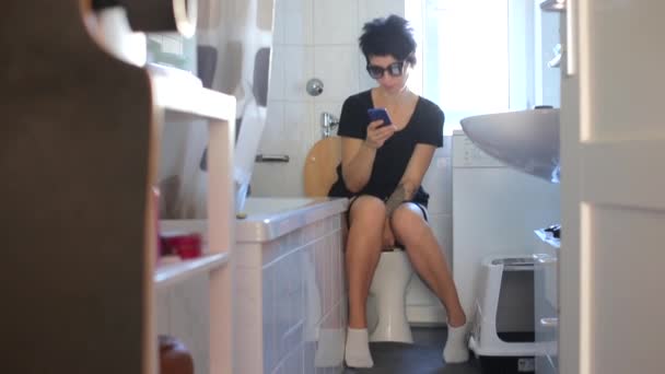 Fille s'assoit sur les toilettes et utilise un smartphone — Video