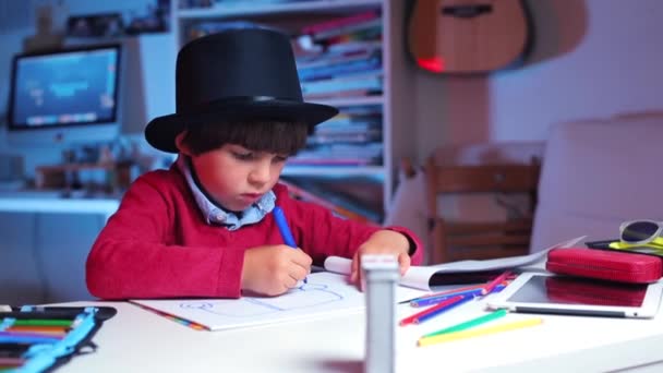Dziecko w czarnym kapeluszu rysuje przy stole — Wideo stockowe