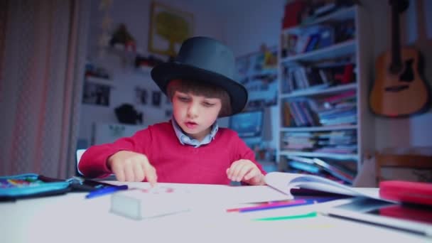 Child, magician, in a hat at the table makes movements with his hands — Stock Video