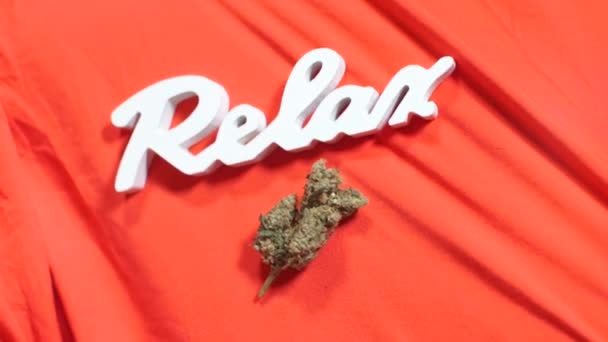 Letras blancas relajarse y brote de cannabis en tela roja — Vídeo de stock