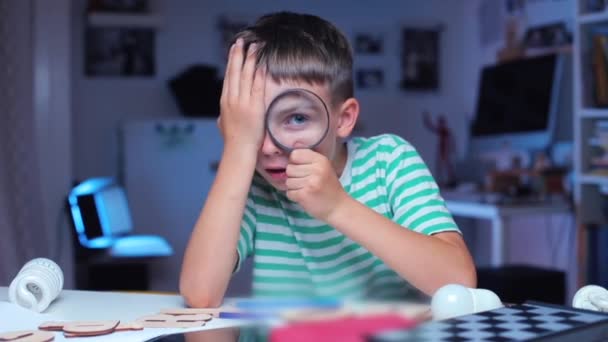 Petit garçon assis à une table, regarde à travers la loupe — Video