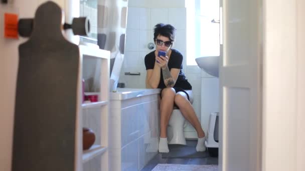 Mädchen benutzt eine mobile Anwendung, während sie auf der Toilette im Badezimmer sitzt — Stockvideo