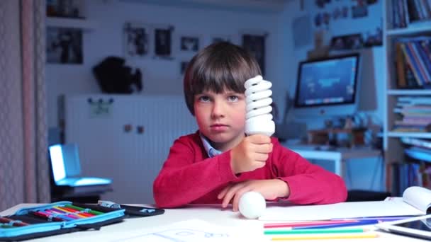 Школьник демонстрирует лампочки, которые он держит в руках — стоковое видео