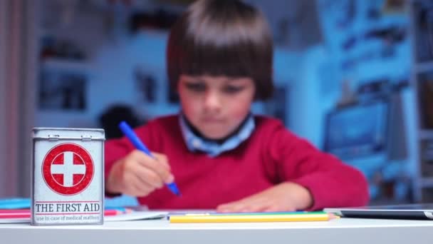 There is a first-aid kit on the table, in the background the boy draws — Stock Video