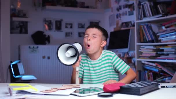 Мальчик кричит в мегафоне, сидит за столом школьного кабинета — стоковое видео