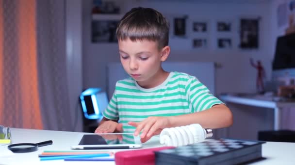 Pojke använder en tablett och undersöker en glödlampa — Stockvideo
