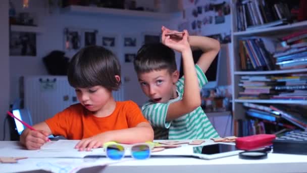 Dos hermanos están sentados en la mesa, uno está dibujando, a continuación mostrando la carta — Vídeos de Stock