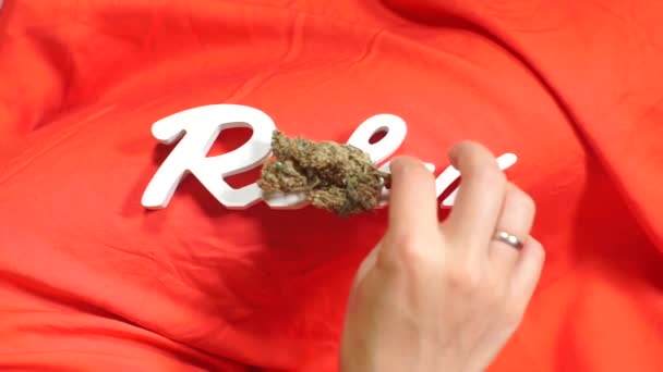 Relajar la inscripción en tela roja, la mano pone un cono de cannabis en la inscripción — Vídeo de stock
