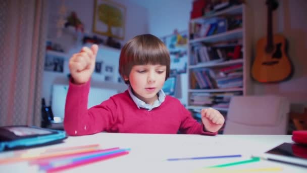 L'enfant s'assoit à une table, prend un crayon et commence à dessiner — Video