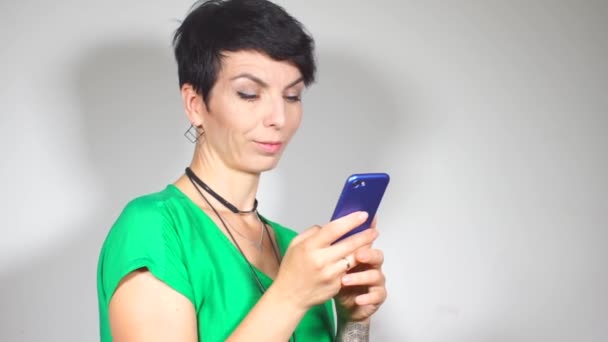Дівчина в зеленій блузці позує зі смартфоном в руках — стокове відео