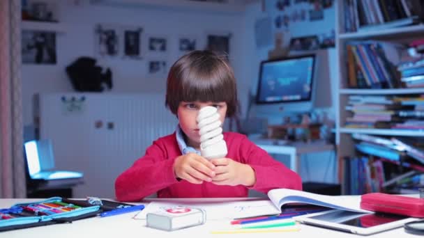 Pojke studier, anser en energibesparande glödlampa — Stockvideo