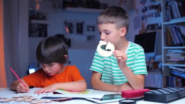 Two schoolchildren are sitting at a table, one draws, second shows the alphabet — ストック動画