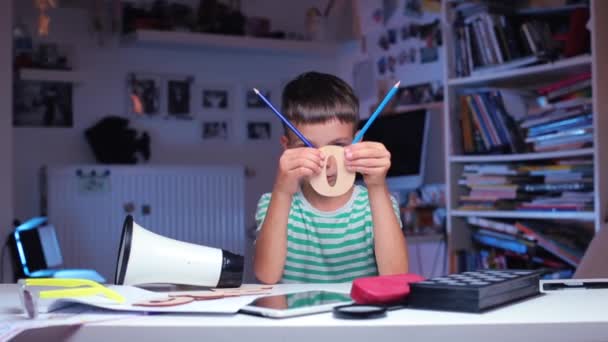 Ragazzo siede a un tavolo, mostra la lettera o con matite — Video Stock