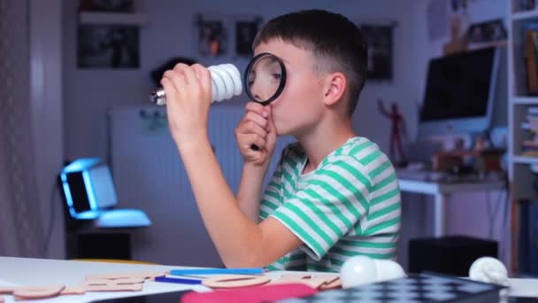 Un niño examina una bombilla a través de una lupa — Vídeos de Stock