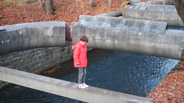 Um adolescente caminha ao longo de uma fina viga acima de um rio em uma cidade . — Vídeo de Stock