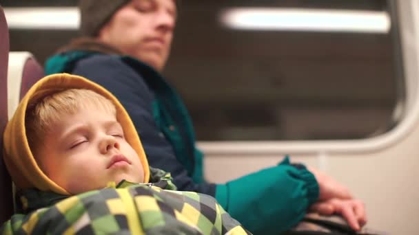 Um rapaz anda de metro com o pai. Um menino sentado em um assento está dormindo — Vídeo de Stock