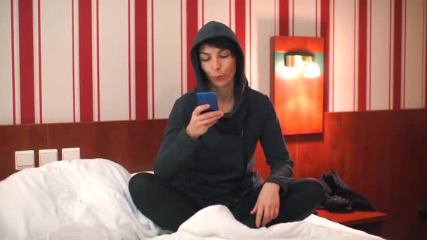 Menina sentada na cama usa um smartphone . — Vídeo de Stock