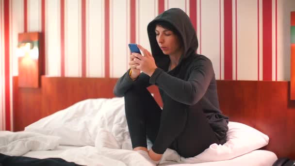 En glad kvinna sitter på en säng på ett hotell.. — Stockvideo