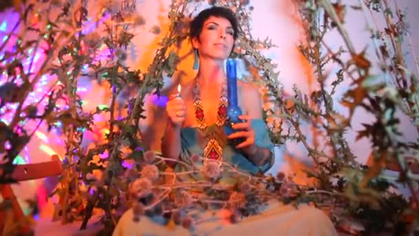 Una chica hippie se sienta en plantas silvestres y espinosas. sosteniendo una pipa en sus manos . — Vídeos de Stock