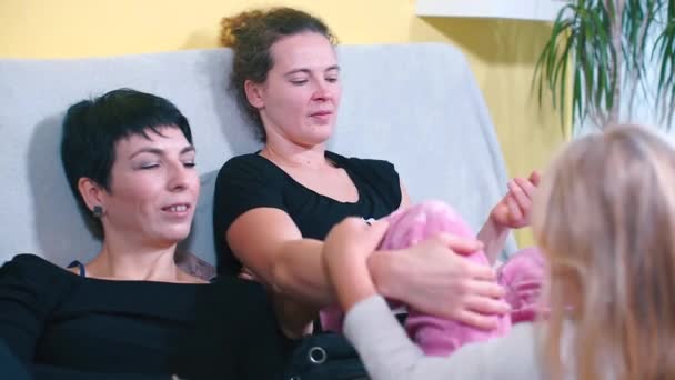 Duas irmãs estão deitadas no sofá em casa e conversando com sua filha . — Vídeo de Stock