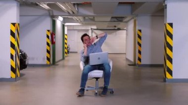 Ofis çalışanı garajda koltukta otururken telefonla konuşuyor..