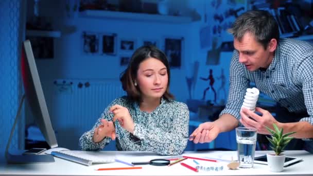 Cara mostra a menina uma lâmpada de poupança de energia poderosa moderna, olha para a câmera — Vídeo de Stock