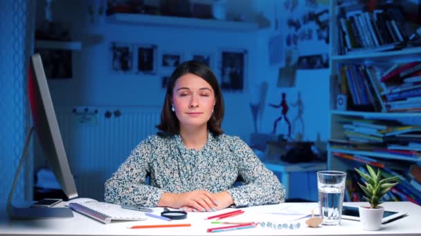 Une fille s'assoit à une table sans mouvement dans le bureau, regardant la caméra . — Video