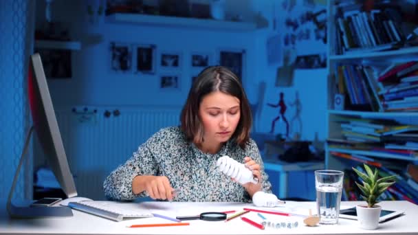 Chica sentada en una mesa examina bombillas — Vídeos de Stock