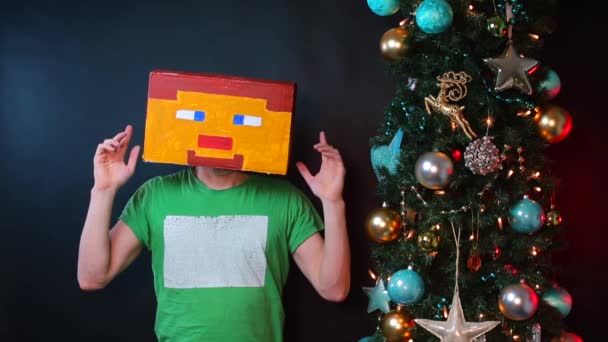 Ein Mann mit bemalter Maske auf dem Kopf sitzt neben einem Weihnachtsbaum. — Stockvideo