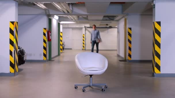 En man kommer med en bärbar dator på en vit stol i garaget. — Stockvideo